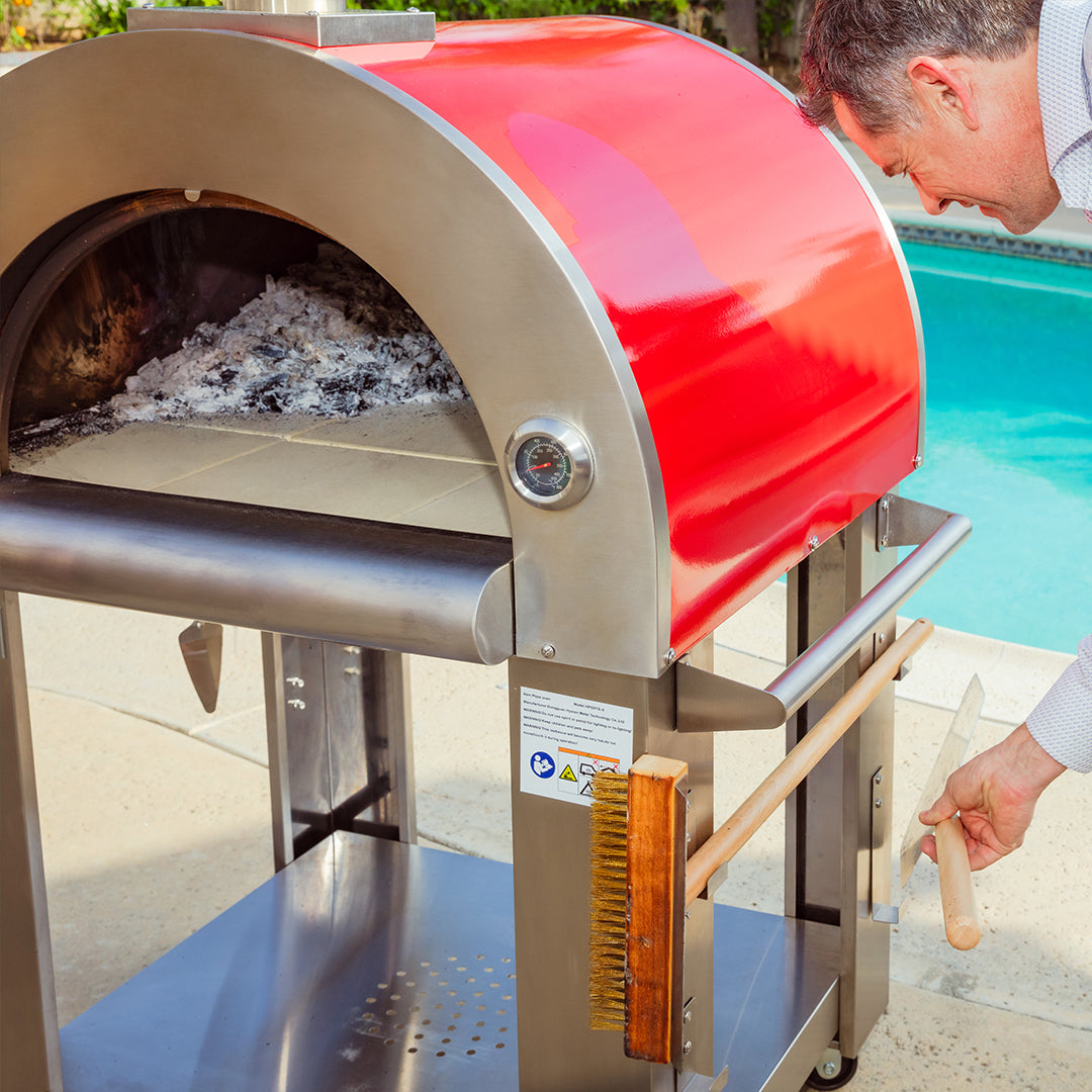 Person using a red and silver outdoor pizza oven by a pool. Empava outdoor wood-fired pizza oven — unique BBQ and cooking gift for dad